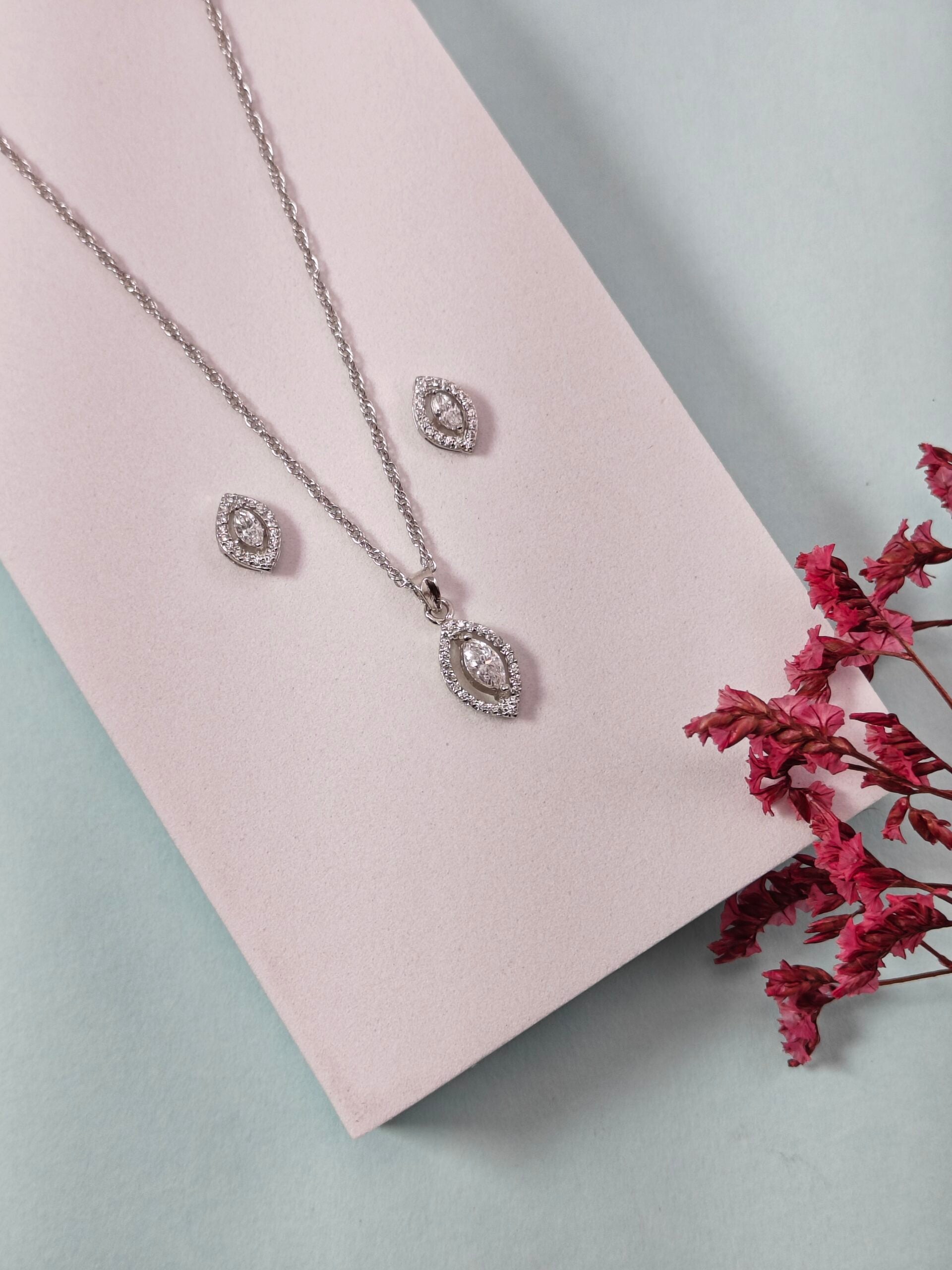 Silver necklace and earrings on a pink card with dried pink flowers on a light blue background